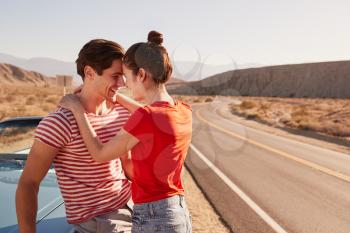 Young white couple embracing by their car at the roadside