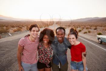Four friends on a desert highway smiling to camera, close up