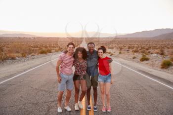 Four friends standing on a desert highway smiling to camera