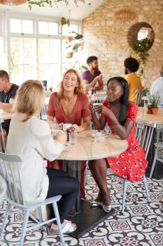 Three female friends talking over brunch at a cafe, vertical