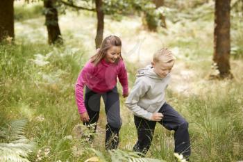 Two children walking together in a forest amongst greenery, three quarter length, side view
