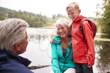 Pre-teen boy standing beside his grandparents, sitting on the shore of a lake, Lake District, UK