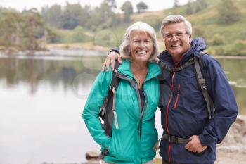 Happy senior couple standing on the shore of a lake smiling to camera, Lake District, UK