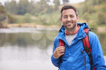 Adult man on a camping holiday standing by a lake smiling to camera, portrait, Lake District, UK