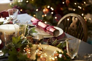Christmas table setting with a Christmas cracker arranged on a plate with red and green table decorations and a Christmas tree in the background