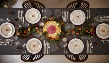 Christmas table setting with baubles arranged on plates and green and red table decorations, overhead view