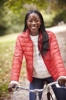 Young adult black woman sitting on a vintage bicycle in a park smiling to camera, front view, close up