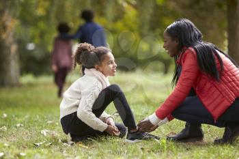 Young black woman helping her daughter to tie her shoes during a family walk in the park, low angle