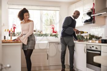 Young mixed race couple preparing Christmas dinner in the kitchen, the man pouring glasses of champagne