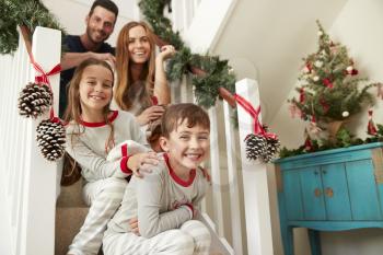 Portrait Of Excited Family Wearing Pajamas Sitting On Stairs On Christmas Morning