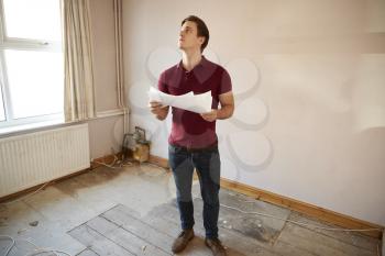 Male First Time Buyer Looking At House Survey In Room To Be Renovated