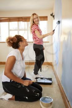 Two Women Decorating Room In New Home Painting Wall
