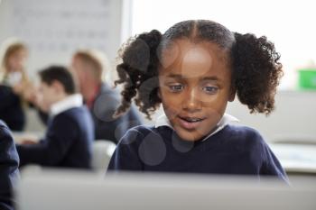 Young black schoolgirl using a laptop computer sitting at desk in a primary school classroom, front view, close up