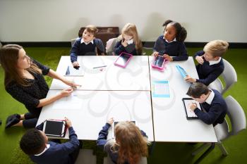 Elevated view of primary school kids sitting around a table in the classroom with their female teacher