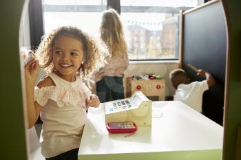 Two young schoolgirls and a boy playing together in a playhouse at infant school, backlit