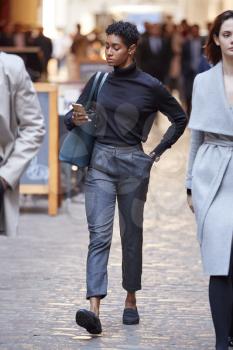 Young black businesswoman walking in the street in London using smartphone, selective focus