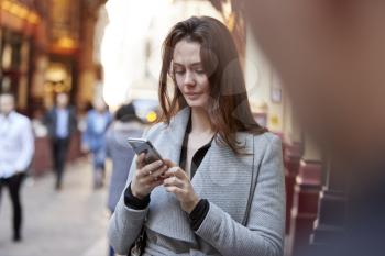 Young white businesswoman standing on a busy London street using smartphone, close up, selective focus
