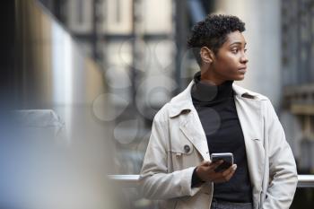 Young black businesswoman standing in the city with smartphone in hand, close up, selective focus