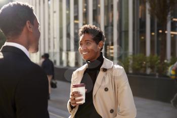 Young black businesswoman standing on the street with a takeaway coffee, talking to her male colleague, selective focus