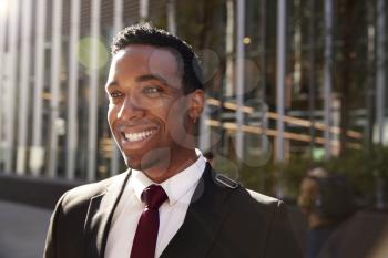 Young black businessman wearing black suit standing on the street smiling, close up with lens flare