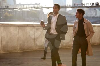 Two business colleagues walking by the Thames riverside in the city of London talking, man holding takeaway coffee