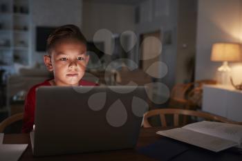 Pre-teen Hispanic boy sitting at dining table doing his homework using a laptop computer, close up