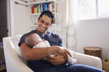 Proud Hispanic father sits holding his four month old son in his arms, horizontal