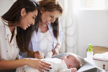 Young Hispanic grandmother and adult daughter playing with her baby son on changing table, close up
