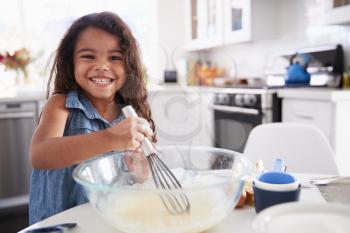 Young Hispanic girl making cake mix in the kitchen on her own, smiling, close up