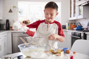 Pre-teen boy adding flour to cake mix in the kitchen on his own, smiling, close up