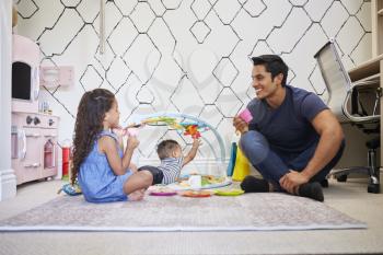 Young girl playing tea party with dad, sitting on the floor, baby brother on a play mat beside them