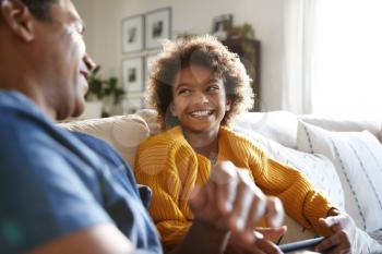 Close up of father and daughter sitting on sofa in the living room looking at each other and laughing, selective focus