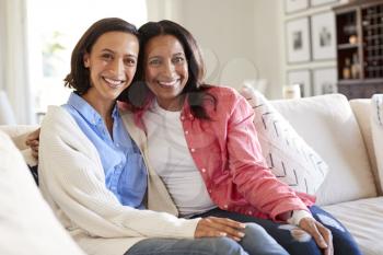 Young adult woman sitting on the sofa in living room with her mother smiling to camera