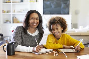 Middle aged mixed race woman sitting at table in her dining room drawing with her pre-teen granddaughter, smiling to camera, front view, close up