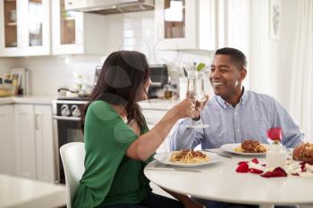 Middle aged mixed race couple making a toast over a romantic meal in their kitchen, close up