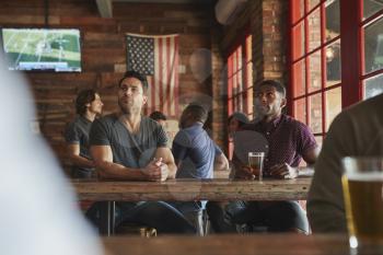 Male Friends Drinking Beer And Watching Game On Screen In Sports Bar