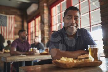 Portrait Of Man In Sports Bar Eating Burger And Fries