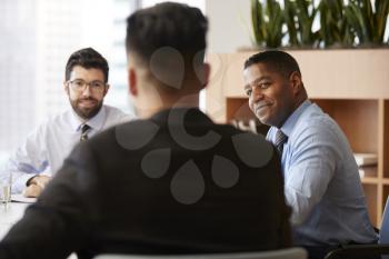 Three Businessmen Sitting Around Table Meeting In Modern Open Plan Office