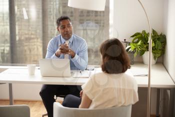 Male Financial Advisor In Modern Office Sitting At Desk Meeting Female Client