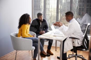 Couple Having Consultation With Male Doctor In Hospital Office