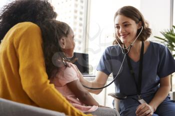 Female Pediatrician Wearing Scrubs Listening To Girls Chest With Stethoscope In Hospital Office