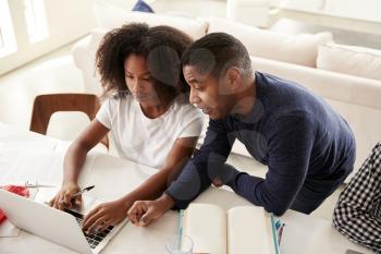 Teenage black girl doing homework with help from her dad, looking at computer screen, elevated view
