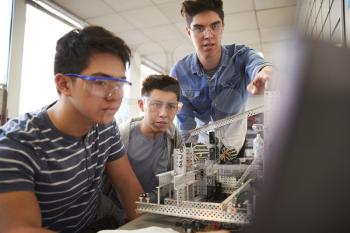 Teacher With Two Male College Students Building Machine In Science Robotics Or Engineering Class