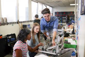 Teacher With Two Female College Students Building Machine In Science Robotics Or Engineering Class