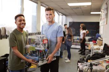 Portrait Of Two Male University Students Carrying Machine In Science Robotics Or Engineering Class