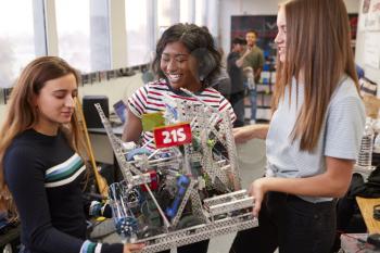 Female University Students Carrying Machine In Science Robotics Or Engineering Class
