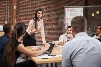 Young Businesswoman Standing And Leading Office Meeting Around Table