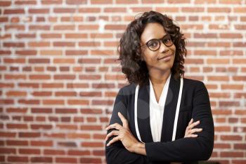 Portrait Of Smiling Businesswoman Wearing Glasses Standing Against Brick Wall In Modern Office