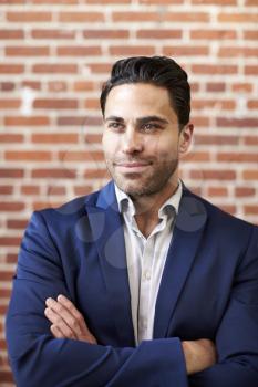 Smiling Mature Businessman Standing Against Brick Wall In Modern Office