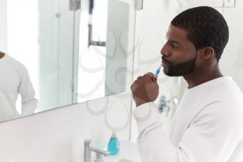 Man Looking At Reflection In Bathroom Mirror Brushing Teeth